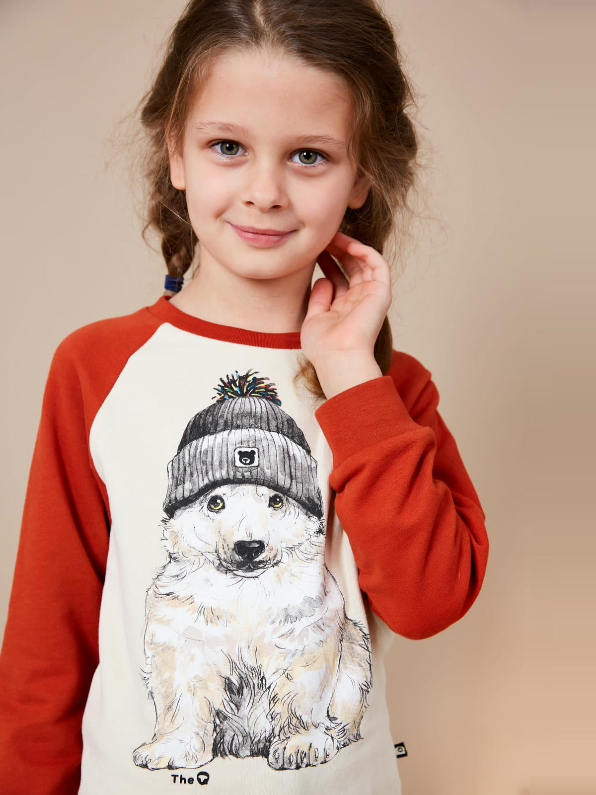 Smiling girl with plaits wearing The QT Beanie Bear organic cotton jumper with rust raglan sleeves