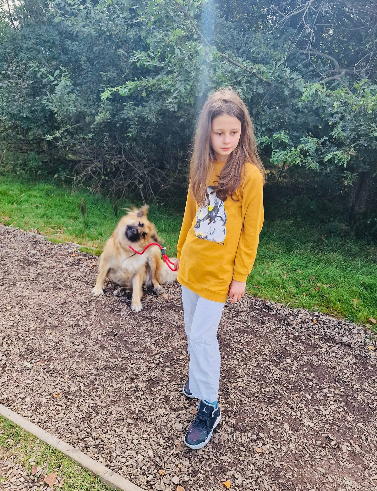 Girl walking her dog on a woodland path in The QT Penguin Cuddle organic cotton jumper dress, worn as a long jumper with trousers