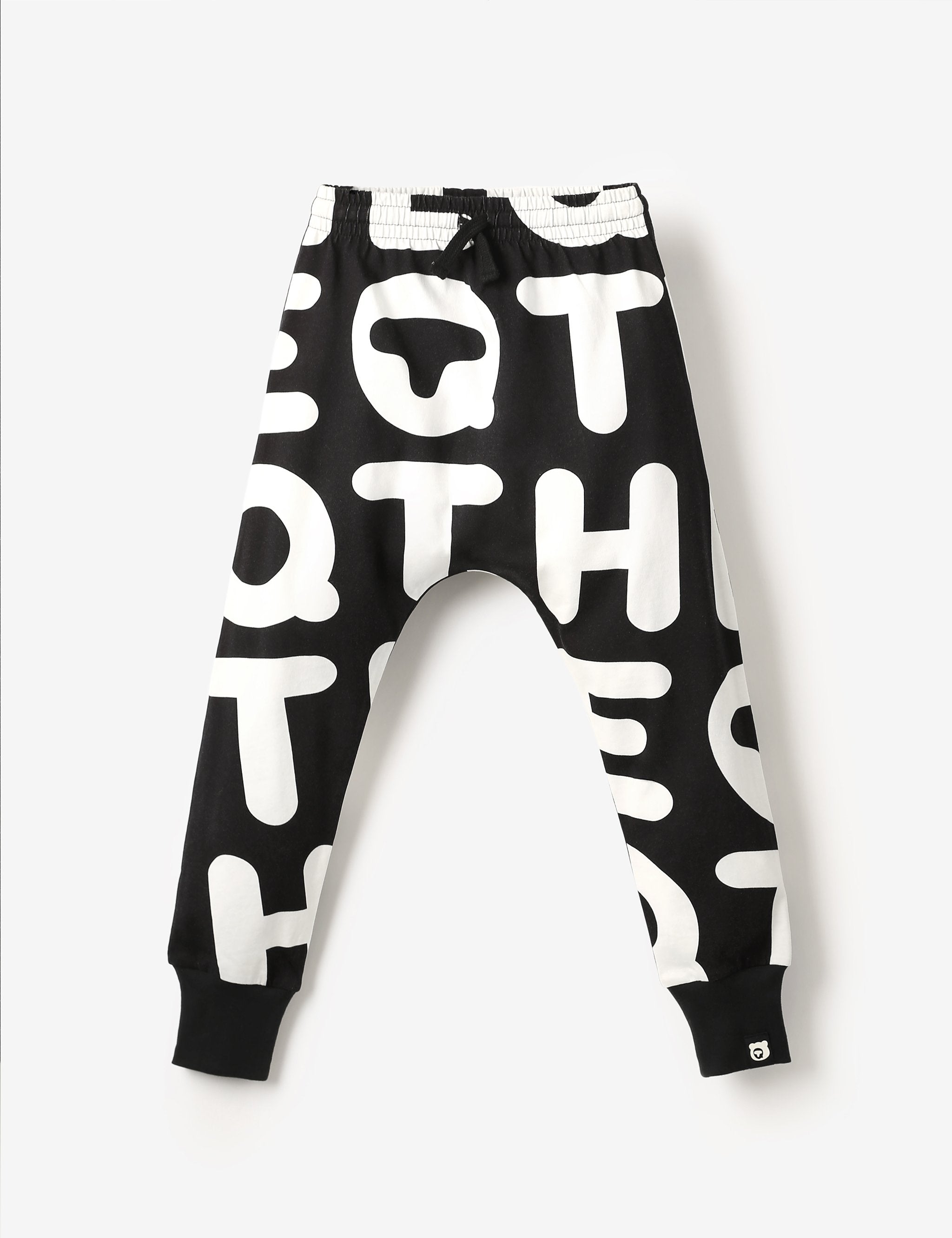 Flat lay of white and black kids joggers with The QT all-over-print, made from soft GOTS-certified organic cotton jersey – unisex, sensory-friendly, comfy and perfect for any adventure.