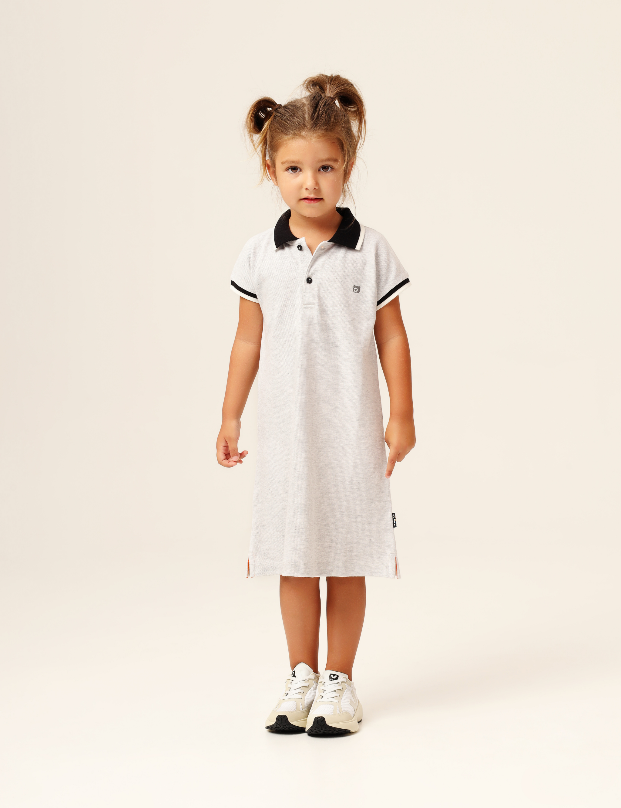 Child wearing organic cotton polo-style dress in grey marl with black and white collar and sleeve trim – cap sleeves, relaxed fit, plastic-free and hypoallergenic.